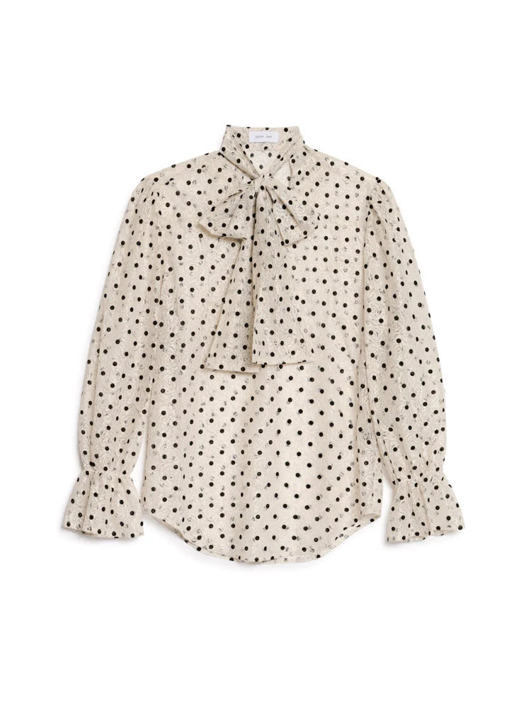 A long-sleeve blouse in cream with a black polka dot pattern, featuring a tie-neck collar and ruffled cuffs, displayed flat against a white background.