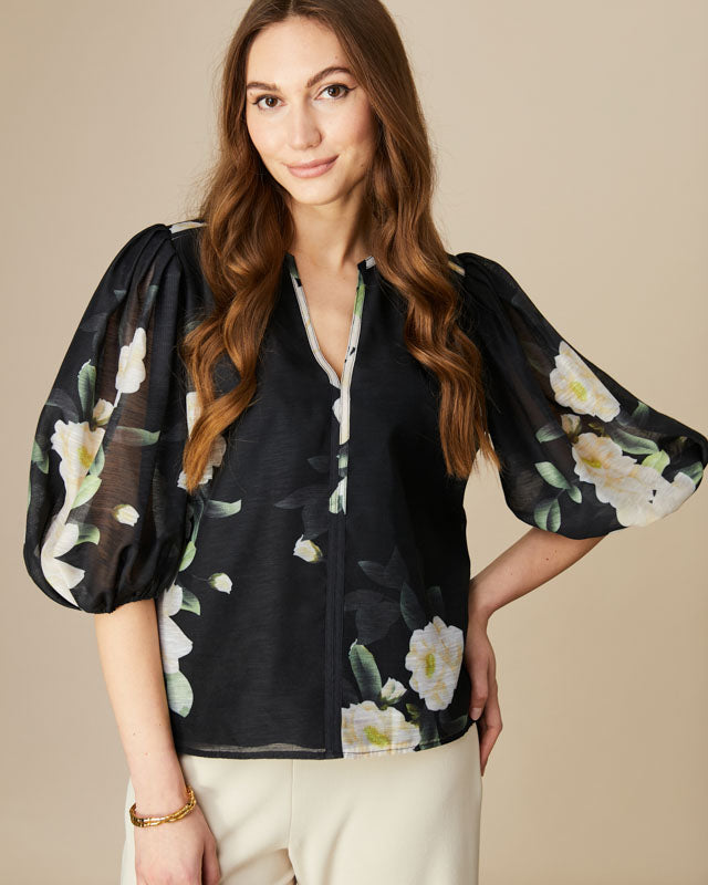Woman wearing a black floral blouse against a beige background